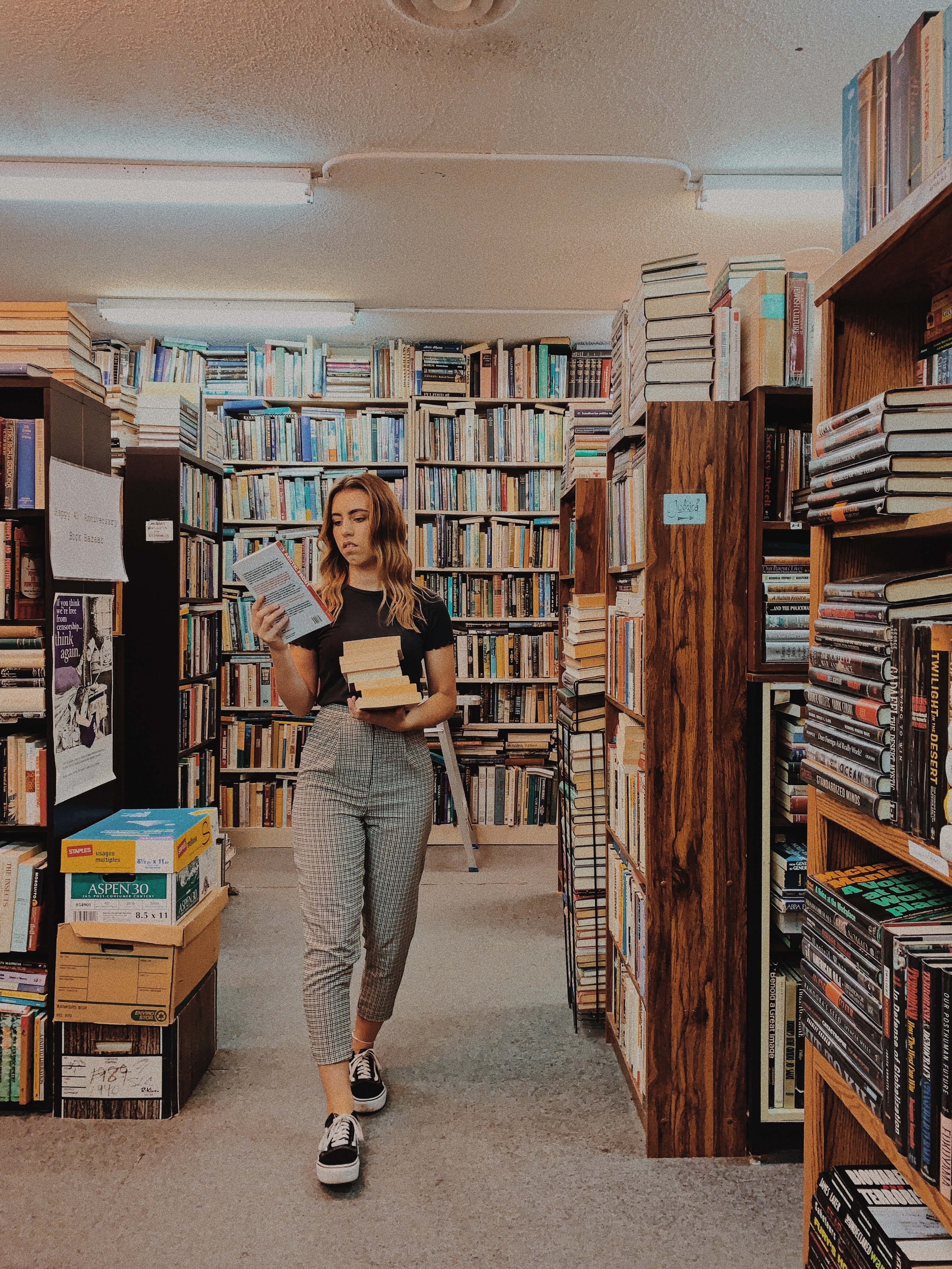 person holding books while walking between bookshelves.